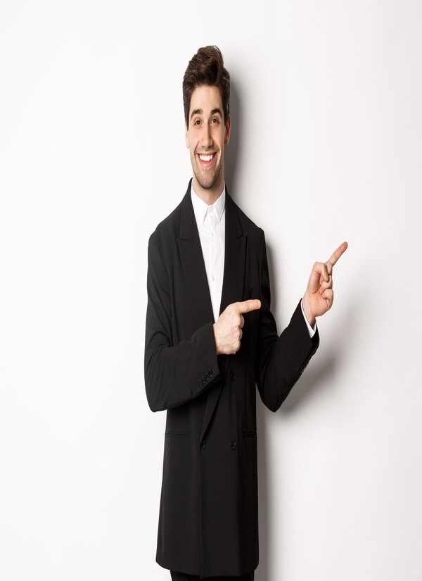Image of attractive smiling guy dressed for new year party, pointing fingers right and showing advertisement, standing over white background.